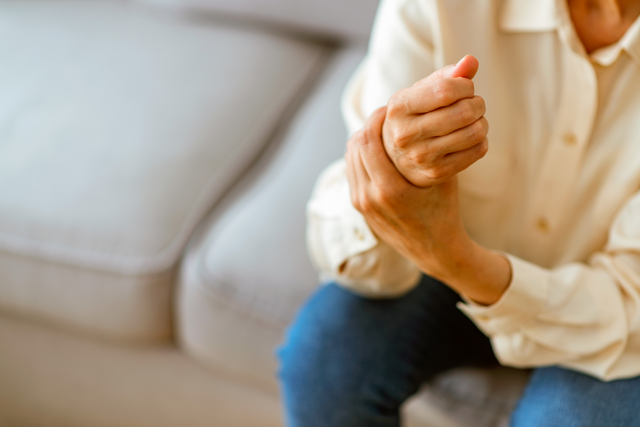 A person sitting on a couch, holding their wrist.